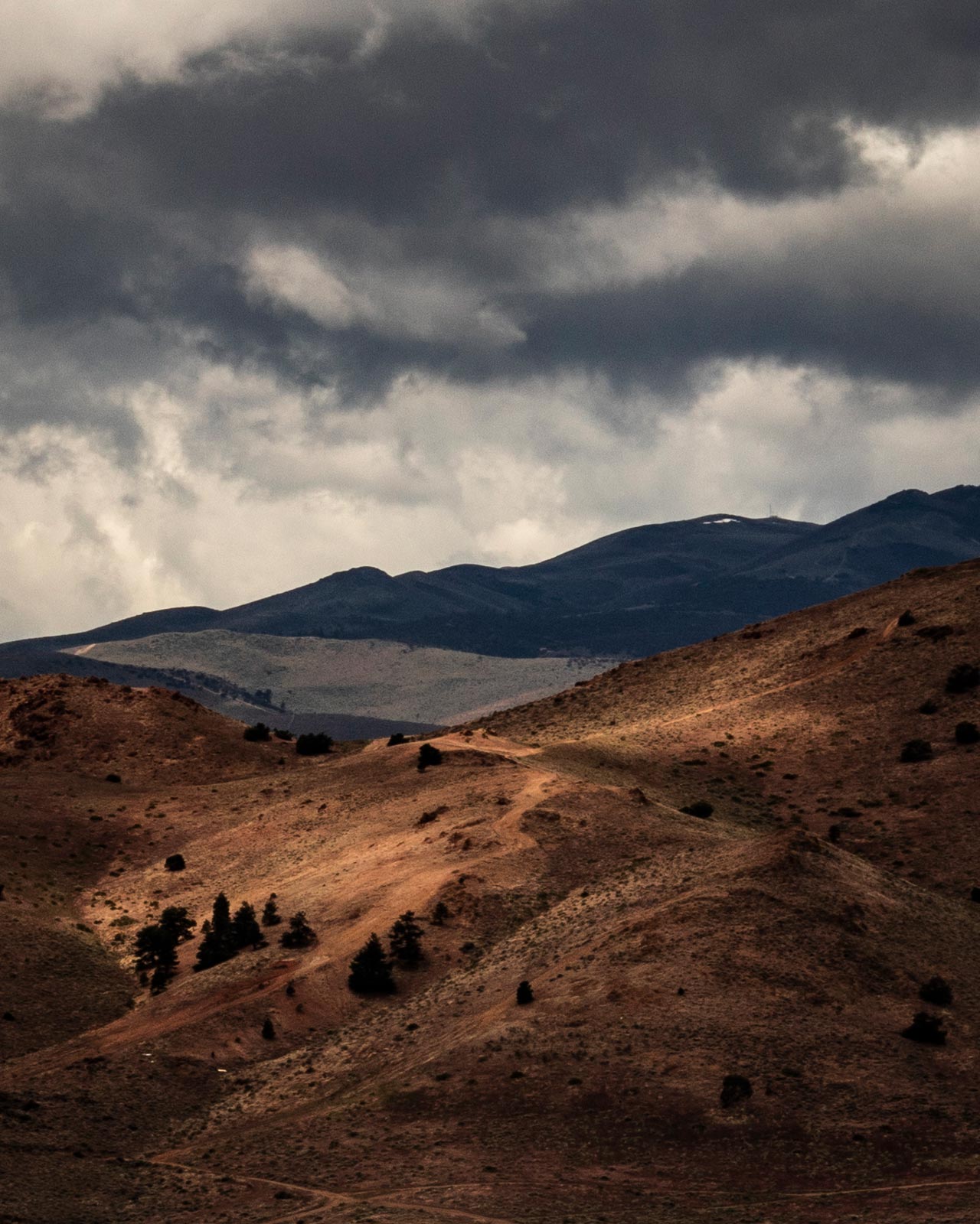 Dark, crunchy clouds move over a stark desert landscape with spots of sunlight breaking through the cloud layer.