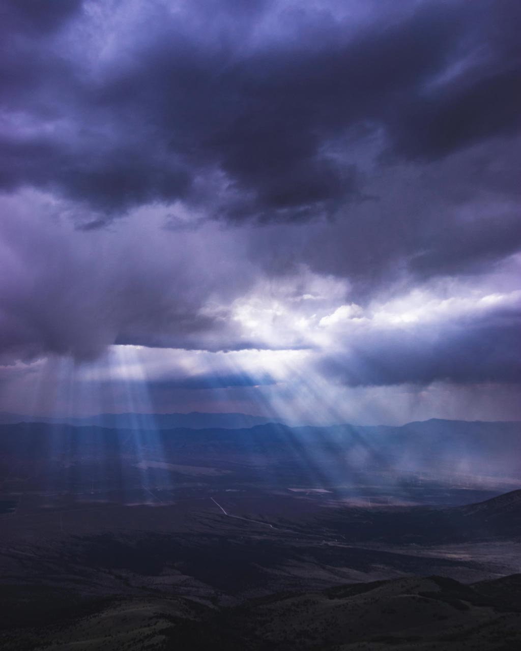 Storm clouds roll through Spring Valley Nevada as sun beams cut through the cloud layer shimmering on rainfall in the distance.